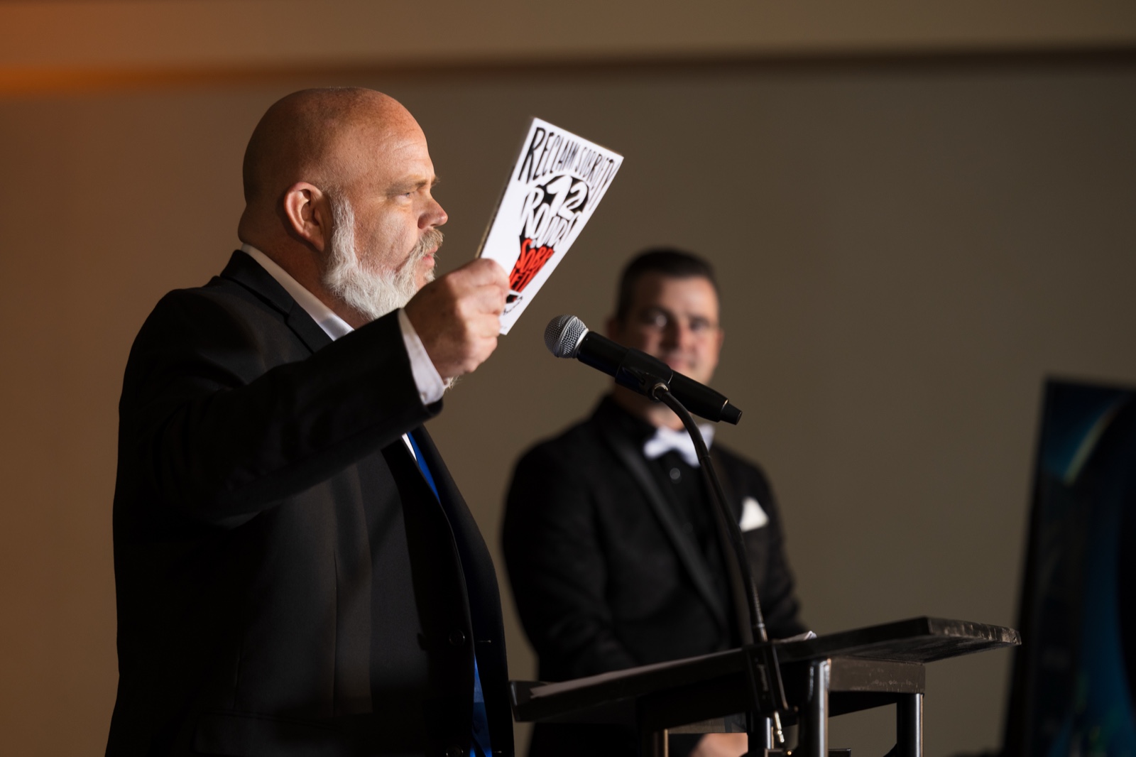 Ken Cox speaking while holding Reclaim Sobriety: The 12 Rounds of Sobriety